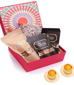 Red hamper box of kaju katlis, crunchy coated cashews, crunchy coated peanuts, butter chakli sticks and t-lites