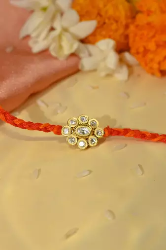 Orange thread floral rakhi with shimmering stone centrepiece
