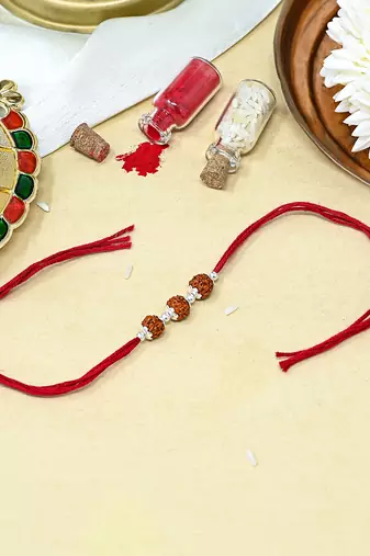 Red thread rakhi with three rudraksha beads and silver accents
