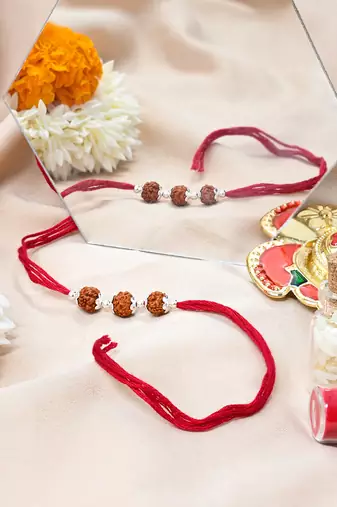 Red thread rakhi with three rudraksha beads and silver accents