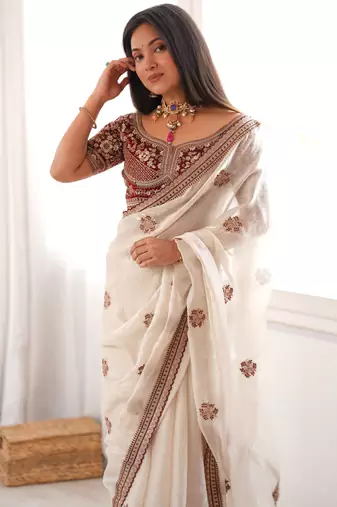 Cream tissue satin embroidered saree with unstitched blouse piece.
