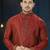 Rust-red kurta with a subtle all-over pattern and ornate gold-toned trim along the collar, placket and cuffs