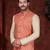 Coral-red and gold patterned nehru jacket paired with an ivory kurta and trousers—an elegant festive ensemble.