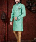 Mint-green patterned sherwani with teal trim, embellished pocket square, and gold trousers.