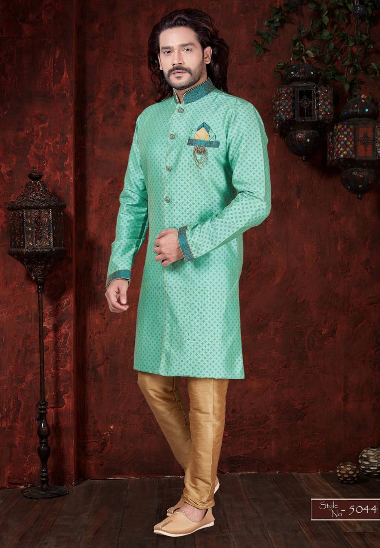 Mint-green patterned sherwani with teal trim, embellished pocket square, and gold trousers.