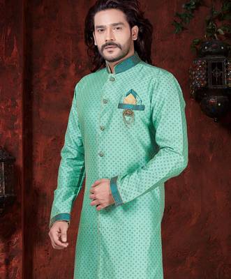Mint-green patterned sherwani with teal trim, embellished pocket square, and gold trousers. 2