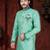 Mint-green patterned sherwani with teal trim, embellished pocket square, and gold trousers.