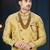 Mustard floral sherwani with pearl accessories, embellished pocket, and gold trousers.