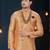 Peach jacquard sherwani with pearl accessories, burgundy pocket, and gold trousers.