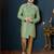 Mint-green patterned sherwani with asymmetrical front, gold pocket square, and gold trousers.