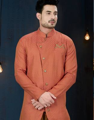 Coral-peach sherwani with textured finish, asymmetrical hem, pocket square, and gold trousers. 2
