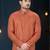 Coral-peach sherwani with textured finish, asymmetrical hem, pocket square, and gold trousers.