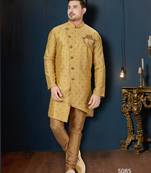 Mustard-gold sherwani with subtle motifs, ornate buttons, chain pocket detail, and gold trousers.