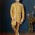 Mustard-gold sherwani with subtle motifs, ornate buttons, chain pocket detail, and gold trousers.