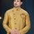 Mustard-gold sherwani with subtle motifs, ornate buttons, chain pocket detail, and gold trousers.