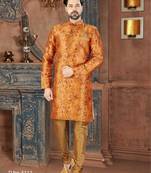 Rust-orange floral sherwani with ornate buttons, matching pocket square, and gold trousers.