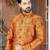 Rust-orange floral sherwani with ornate buttons, matching pocket square, and gold trousers.