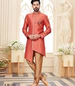 Coral-peach sherwani with gold piping, chain pocket, and gold trousers.