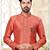 Coral-peach sherwani with gold piping, chain pocket, and gold trousers.