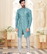 Teal-and-white patterned sherwani with asymmetrical front, matching pocket square, and white trousers.